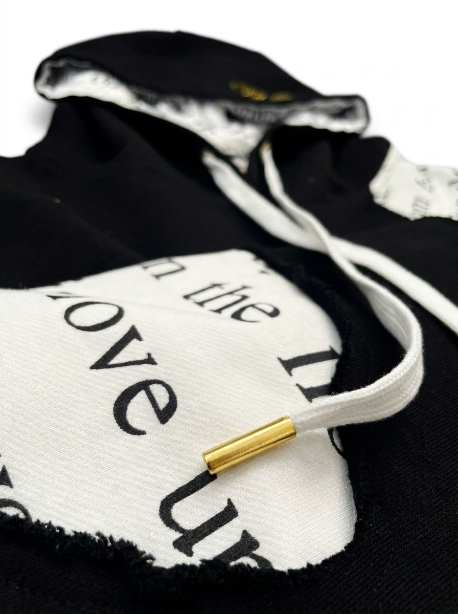 Detail of The Covering Hoodie black drawstring with gold metal aglet against heavyweight black French terry cotton.