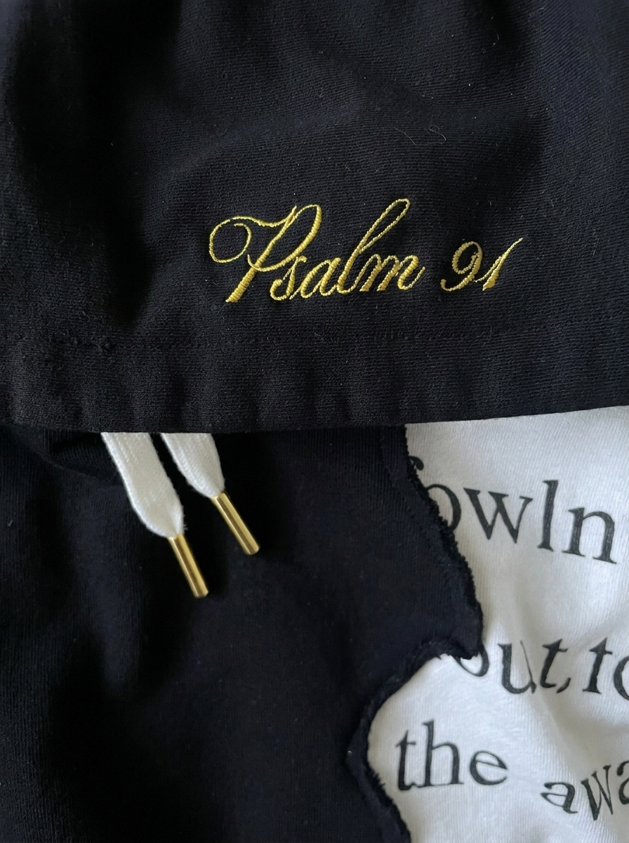 Gold cursive Psalm 91 embroidery on black fabric beside white scripture panel of The Covering Hoodie.