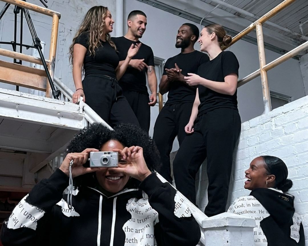Group of people in black outfits with one taking a photo, in an industrial setting.