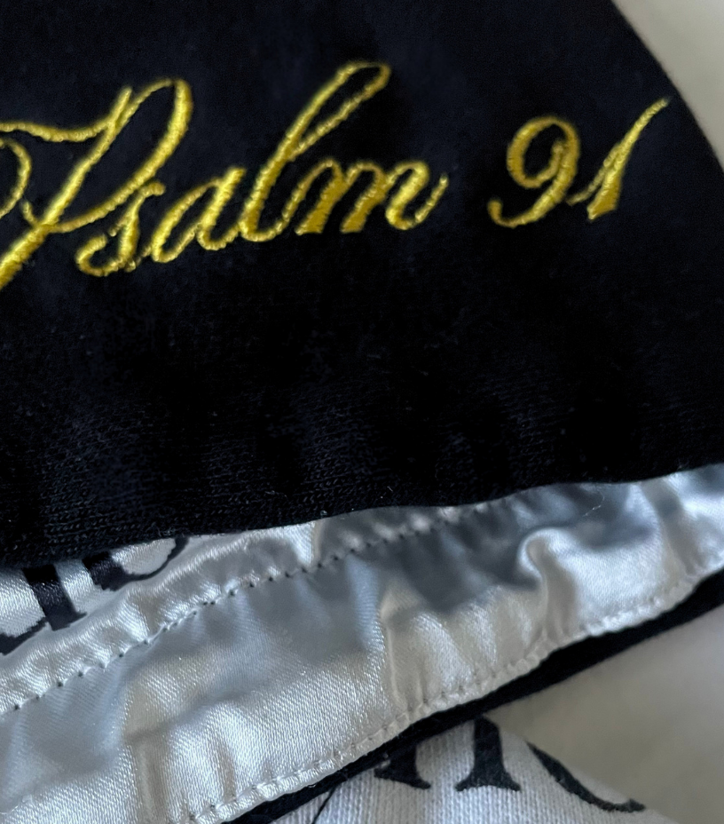 Black fabric with gold embroidery of 'Psalm 91' on a white background