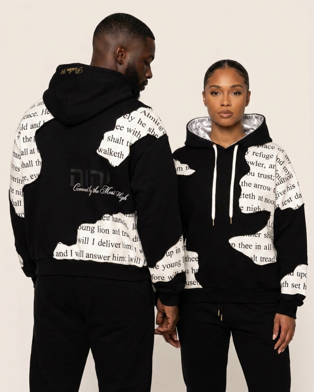 Two people wearing black hoodies with white text design on a beige background
